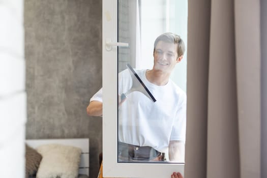 Side view of smiling man with bottle of detergent and rag cleaning window at home.