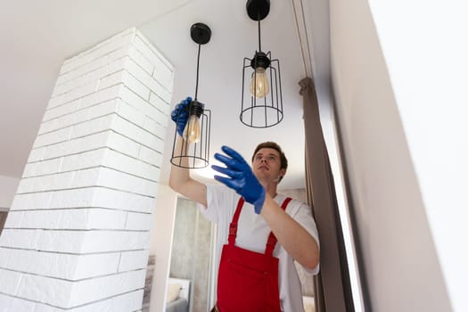 Young man installing ceiling lamp on stepladder in kitchen.