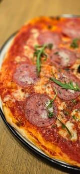 Freshly baked New York style pizza with melted mozzarella cheese and base tomato sauce close-up on a wooden board on the table. with lots of pepperoni