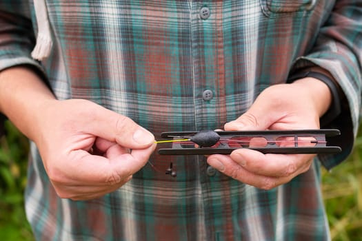 A man in a plaid shirt holds a reel with fishing line, ready to go fishing