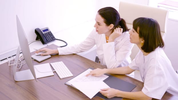 Two female doctor colleagues discussing about medical report using computer in the clinic