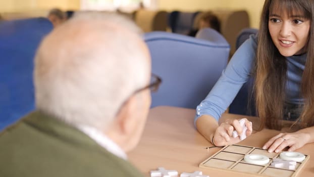 Girl explaining the rules of a game to a senior man in a nursing home