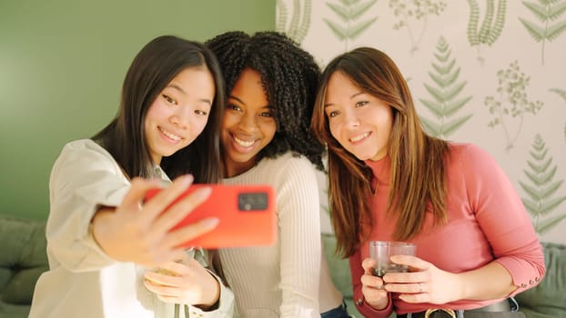 Group of multi-ethnic friends smiling taking a selfie sitting on the sofa at home