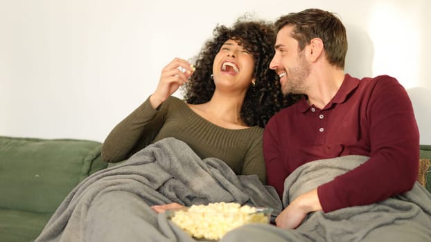 Couple flirting and laughing eating popcorn watching movie at home