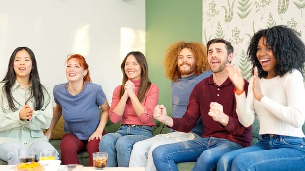 Group of friends celebrating something they are watching on TV while having a drink at home