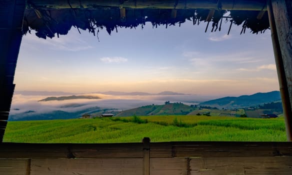 A view of a field with a foggy sky and mountains in the background. The sky is a mix of blue and orange hues, creating a serene and peaceful atmosphere. Rice terrace farm field and mountains.