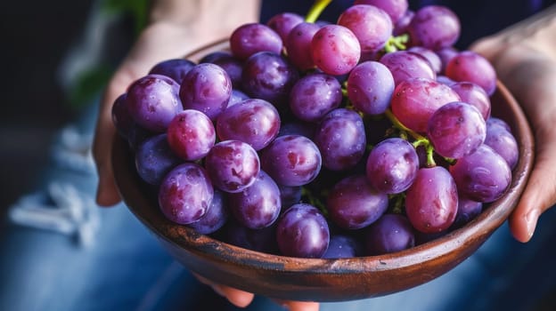 A person holding a bowl of purple grapes in their hands