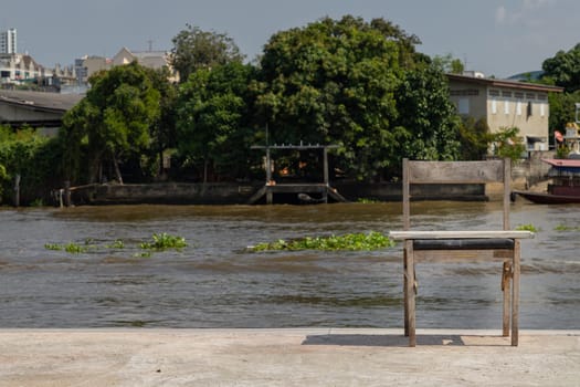 The old wooden chair is in front of the river, which is on the cement floor. Space for text, Selective focus.