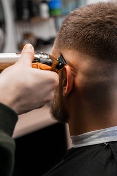 Master trims client hair with professional tool in luxury barbershop closeup. Barber does straight hairdo contour in men beauty salon