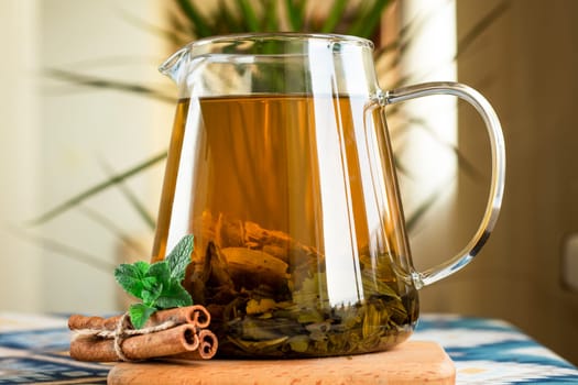 selective focus. Green tea in a teapot with cinnamon sticks and fresh mint. Hot tea in a glass teapot in the kitchen. Large tea leaves. drink with mint and cinnamon.