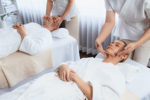 Caucasian couple enjoying relaxing anti-stress head massage and pampering facial beauty skin recreation leisure in dayspa modern light ambient at luxury resort or hotel spa salon. Quiescent