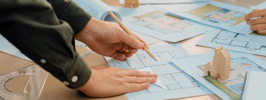 Professional engineer team discussion about house design on meeting table with architectural equipment and blueprint scatter around at modern office. Focus on hand. Closeup. Delineation.