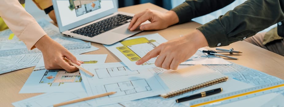 Professional architect shows mistake structure in blueprint while analysis and comparison with picture in laptop on table with blueprint and architectural equipment. Cropped image. Delineation.