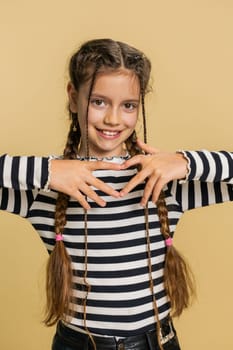 Girl in love. Smiling attractive young preteen child kid makes heart gesture demonstrates love sign expresses good positive feelings and sympathy. Teenager children isolated on beige background