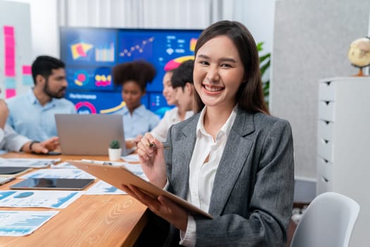 Portrait of happy young asian businesswoman with group of office worker on meeting with screen display business dashboard in background. Confident office lady at team meeting. Concord