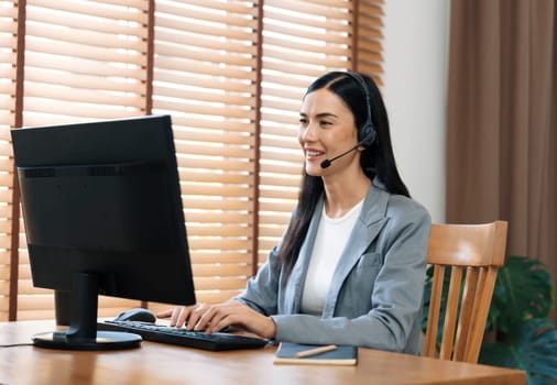 Female call center operator or customer service helpdesk staff working on workspace while talking on the headset to provide assistance for customer. Professional modern business service. Blithe