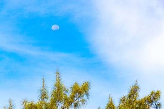 Crescent half full moon in the blue sky during the day with clouds in Playa del Carmen Quintana Roo Mexico.