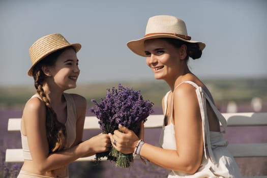 A woman and a child are sitting on a bench in a field of purple flowers lavande. The woman is holding a bouquet of flowers and the child is holding a bouquet of flowers as well.