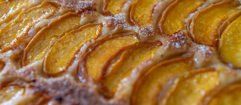 A close up of a dessert made of sliced peach. The dessert is covered in a caramel glaze and has a golden brown crust. The peach are arranged in a spiral pattern, creating a visually appealing.