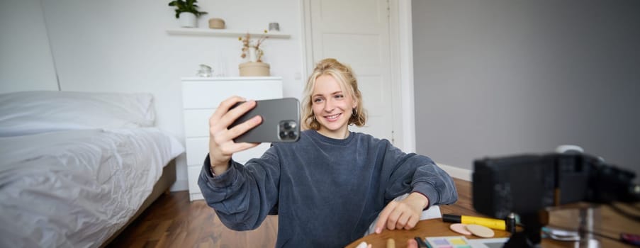 Portrait of young woman, girl beauty blogger, recording vlog in her bedroom, doing makeup tutorial for social media followers, taking selfies, live streaming on mobile phone app.