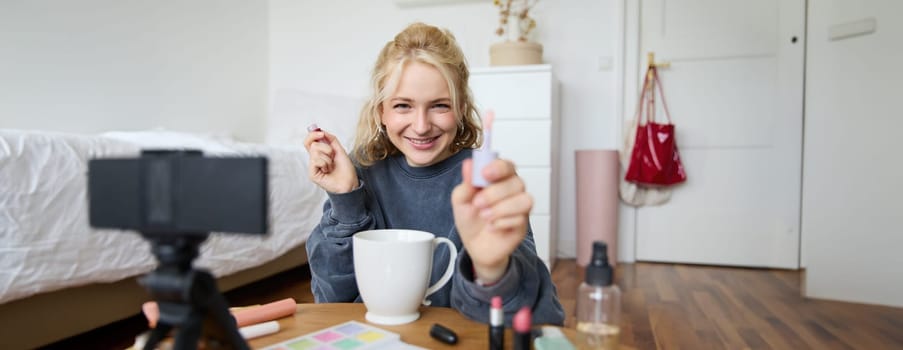 Lifestyle, beauty blogger, woman recording video of her putting on makeup, talking to camera, making online tutorial, showing her lip gloss or lipstick to followers, sitting on floor with cup of tea.