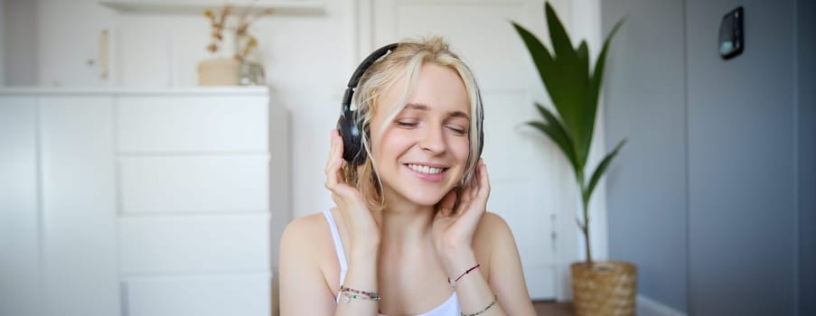 Concept of people and lifestyle, Close up of beautiful blond woman in wireless headphones, listens to music, enjoys good quality sound in new earphones.