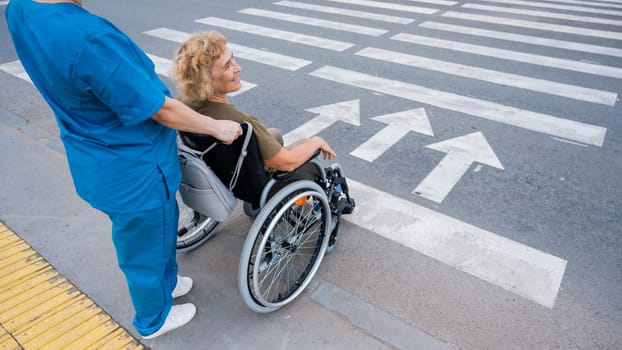 Rear view of a nurse helping an elderly woman in a wheelchair cross the road