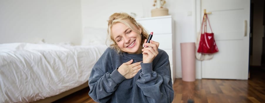 Portrait of young content creator, woman with social media account, recording video about makeup on digital camera, holding favorite lipstick, recommending product to audience online.