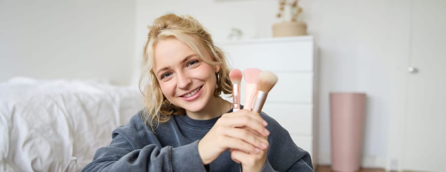 Close up portrait of cute teen girl showing her beauty makeup brushes, smiling and looking at camera.