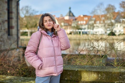 Young beautiful pretty tourist girl in warm hat and coat with backpack walking at cold autumn in Europe city enjoying her travel in Zurich Switzerland. Outdoor portrait of young tourist woman enjoying sightseeing