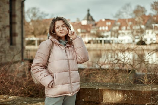 Young beautiful pretty tourist girl in warm hat and coat with backpack walking at cold autumn in Europe city enjoying her travel in Zurich Switzerland. Outdoor portrait of young tourist woman enjoying sightseeing