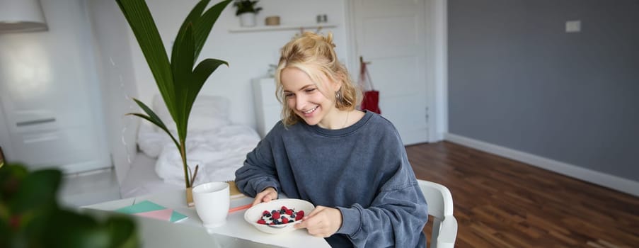 Portrait of young candid girl watching videos on laptop, enjoying movie and eating in front of laptop, having breakfast and staring at screen.