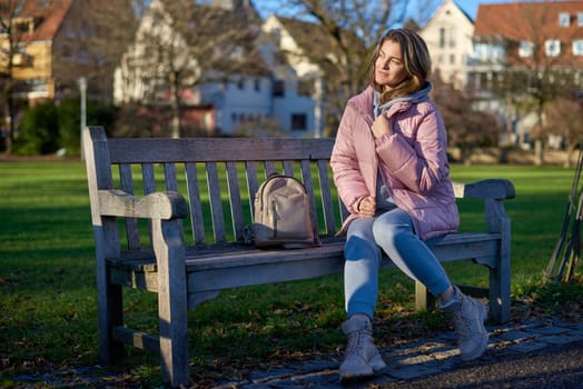 Winter Wonderland Elegance: Beautiful Girl in Pink Jacket Enjoys Festive Atmosphere in Bitigheim-Bissingen Park. Experience the magic of the holiday season as a charming girl in a pink winter jacket sits on a bench in a park against the backdrop of the historic town of Bitigheim-Bissingen, Baden-Württemberg, Germany. The scene is adorned with picturesque half-timbered houses, creating a delightful blend of winter charm and architectural beauty.