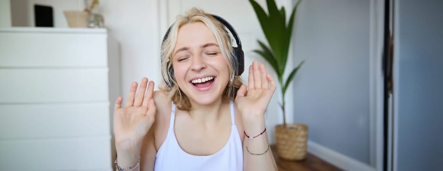 Close up portrait of candid, happy young woman in headphones, singing and listening to music at home.