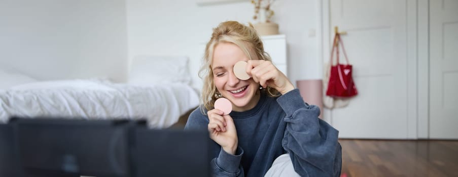 Portrait of beautiful and stylish young woman, vlogger recording video on her digital camera in a room, showing beauty products, making makeup tutorial for followers on social media.