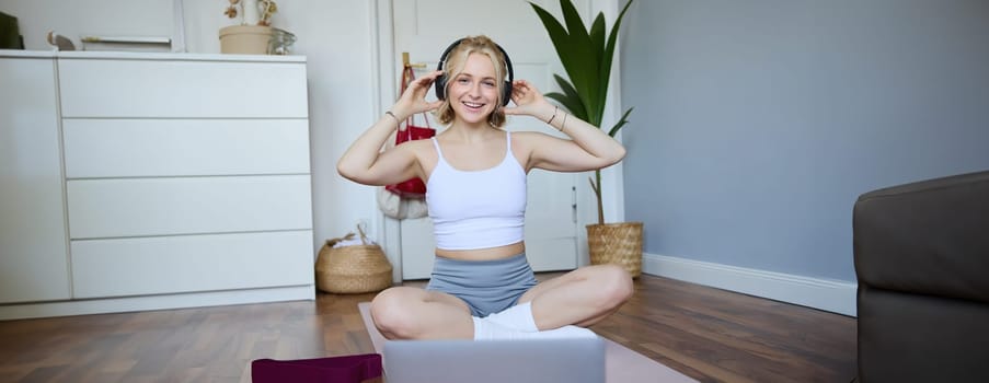 Portrait of fit and healthy young woman in wireless headphones, does workout, using online video tutorials, listens to fitness instructor on laptop, exercising at home.