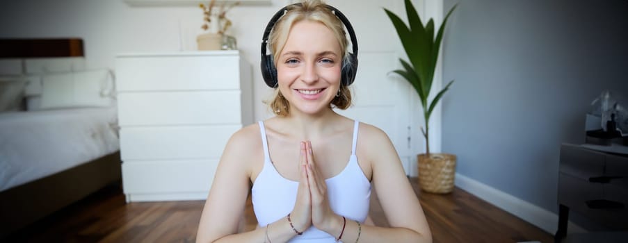 Wellbeing and people concept. Close up portrait of young woman in headphones, meditating, practice yoga, listens to podcast in earphones.