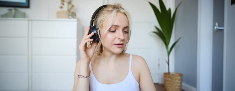 Portrait of good-looking young blond woman in wireless headphones, listens to podcast or favourite song, enjoys music in new earphones.