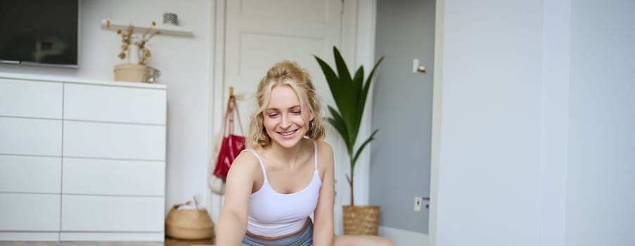 Portrait of young fitness instructor, vlogger creating content at home, doing workout and record exercises on digital camera, using rubber yoga mat.