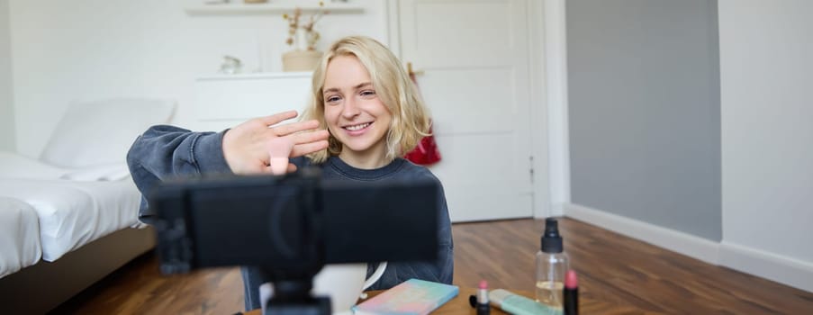 Close up portrait of happy young beauty blogger, records lifestyle vlog in her room, using camera with stabiliser, shows makeup brush and cosmetics.