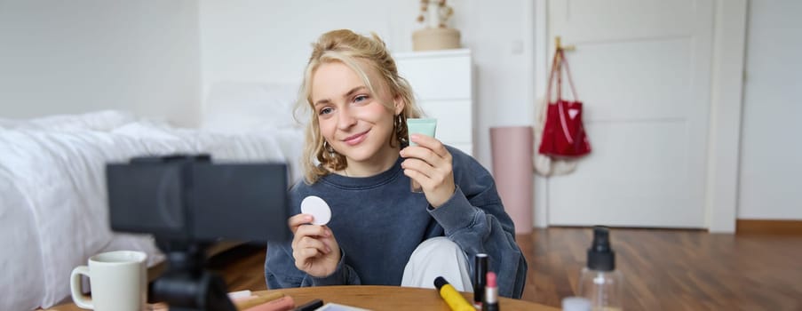 Portrait of young woman promoting beauty product, applies makeup in front of camera, recording video for her vlog, creating content for social media, sitting in a room on floor.