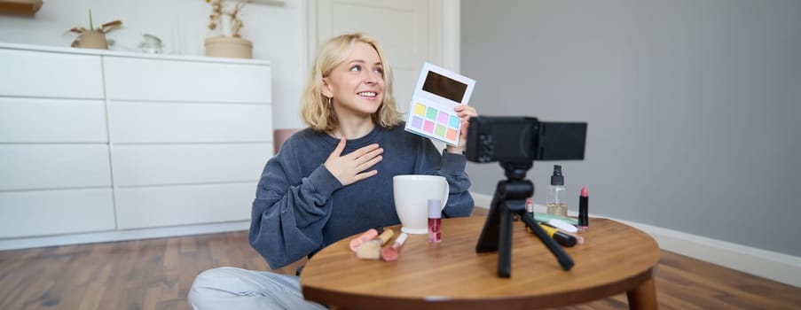 Portrait of beautiful lifestyle blogger, girl records a video on her camera for social media, shows palette of eyeshadows, does a makeup tutorial for her followers, sits in her room.
