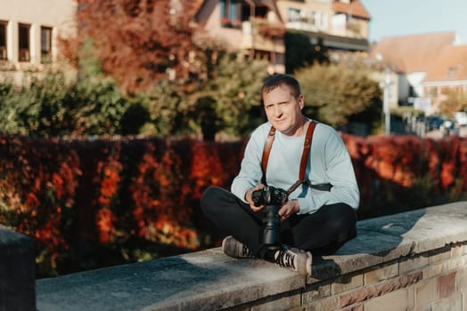 Man Sitting on Stairs in Old European City And Holding Photo Camera. Contemporary Stylish Blogger And Photographer