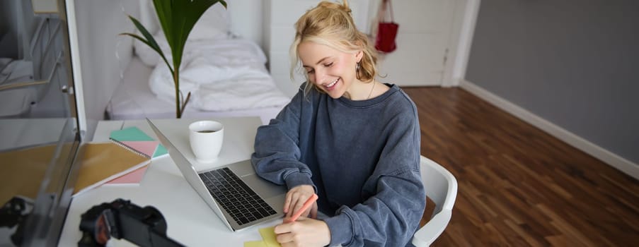 Portrait of young woman distance learning, working from home with laptop, making notes, student studying on remote, doing online course.