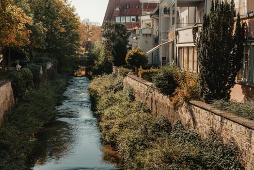 Beautiful small river with clean and clear water front of colorful autumn trees and small old town on the hill agaist nice blue and clouds sky during autumn in Europe.