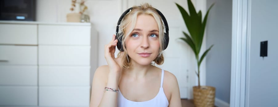 Concept of people and lifestyle, Close up of beautiful blond woman in wireless headphones, listens to music, enjoys good quality sound in new earphones.