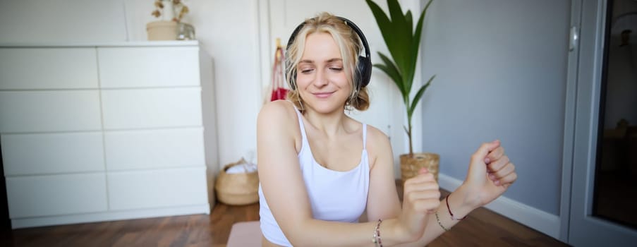 Close up of athletic young woman, cute female model in wireless headphones, dancing to favorite song, listens to music in earphones.