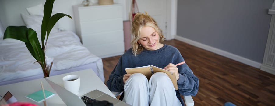 Portrait of cute, smiling young social media content creator, girl records video on digital camera and stabiliser, holds notebook, talks to audience, vlogging in her room.