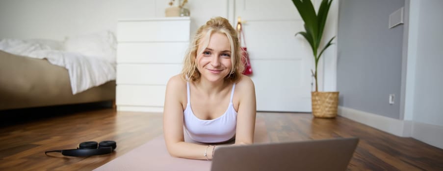 Portrait of young smiling woman doing fitness training, yoga session at home, lying on rubber yoga mat and working out.