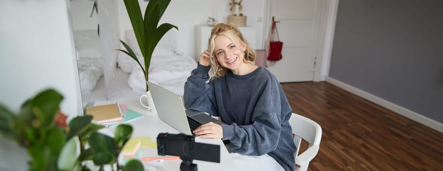Portrait of young beautiful woman, social media influencer, recording video tutorial, lifestyle vlog, creating content in her room using digital camera.